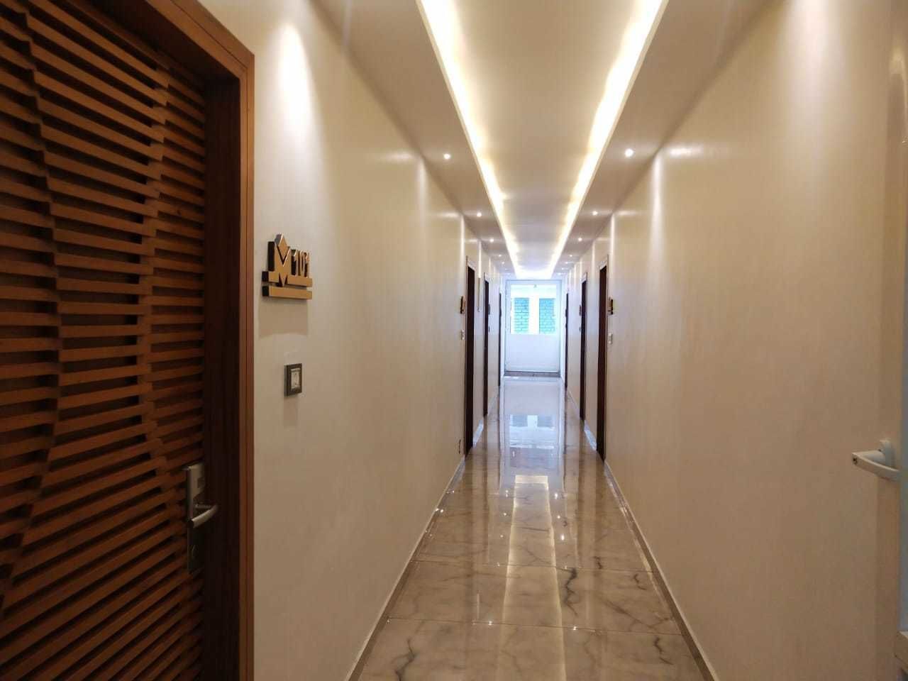 Un couloir avec une porte à lattes de bois sur la gauche, une enseigne portant le mot « Motel » sur le mur et un plafond lumineux doté de spots encastrés.