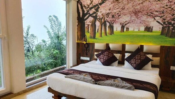 Un dormitorio con una cama grande, vistas a la vegetación a través de una ventana y un cuadro de flores de cerezo en la pared.