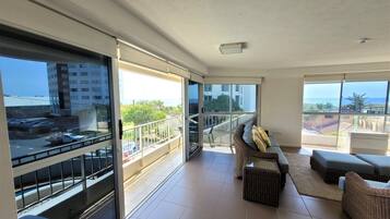 Un vaste balcon offrant une vue sur la ville et la mer, aménagé avec un canapé, un fauteuil et une petite table.