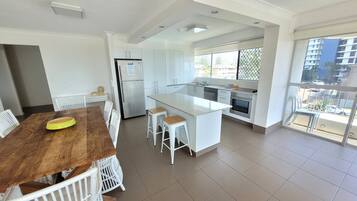 Une cuisine moderne avec des meubles blancs, un îlot central et un coin repas comprenant une table en bois et des chaises blanches.