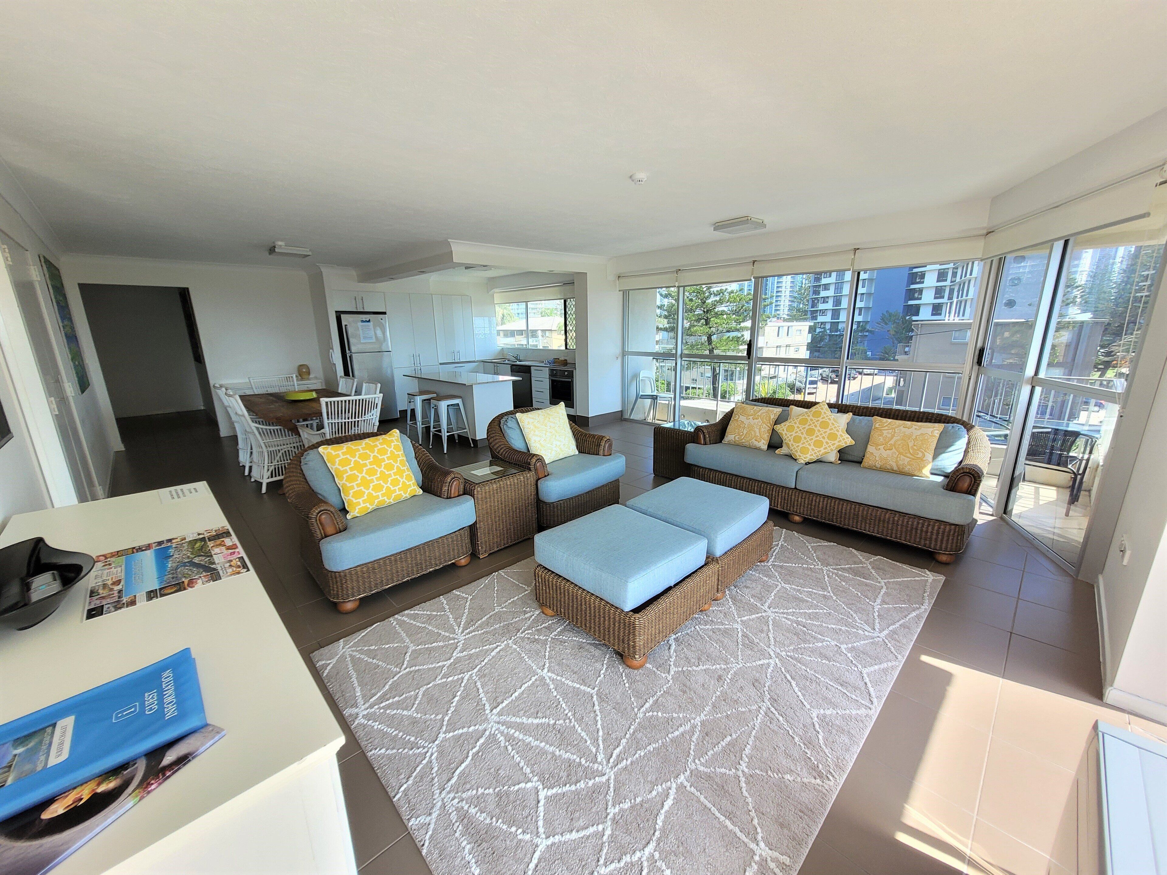 A spacious living area with a large sofa set, a dining table, and a kitchen in the background.