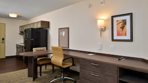 A compact kitchen with a refrigerator, a dining table with chairs, and a wall-mounted lamp.