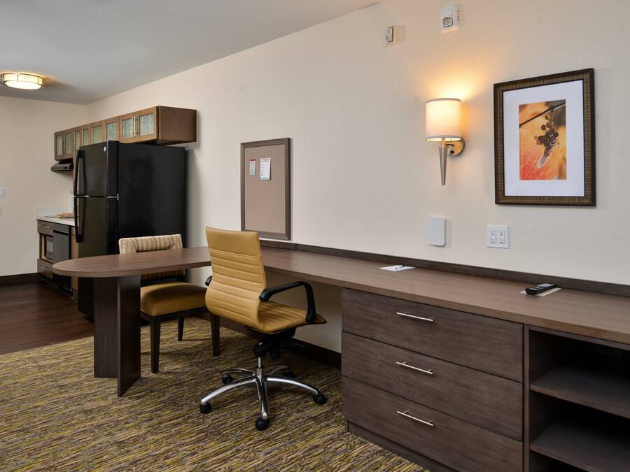 A compact kitchen with a refrigerator, a dining table with chairs, and a wall-mounted lamp.