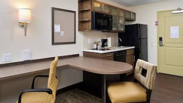 A compact hotel room with a kitchenette, a dining area with a table and two chairs, a light fixture, and a door with a lock.