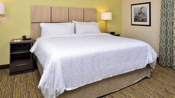 A hotel room with a bed, nightstand, lamp, and a framed picture on the wall.