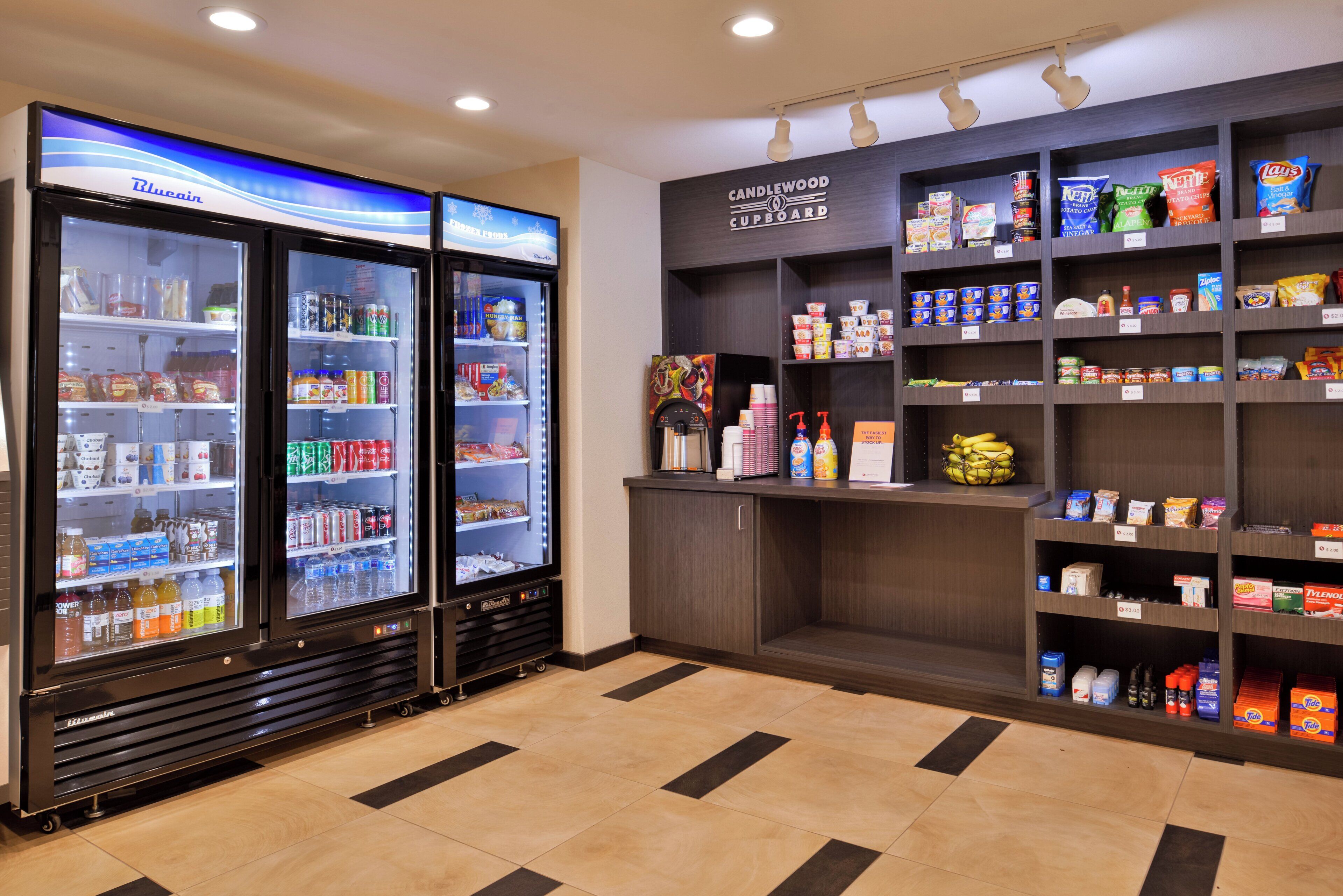 Un área de autoservicio con dispensadores refrigerados de bebidas y una variedad de aperitivos y condimentos en estantes.