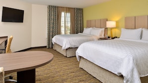 A hotel room with two beds, a desk, a chair, a TV, and a lamp.
