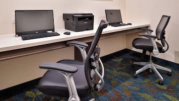 Ein Hotelarbeitsplatz mit zwei Schreibtischen, jeweils mit einem Laptop, einem Drucker und einer Computermaus ausgestattet. Es gibt zwei Bürostühle mit Rollen.