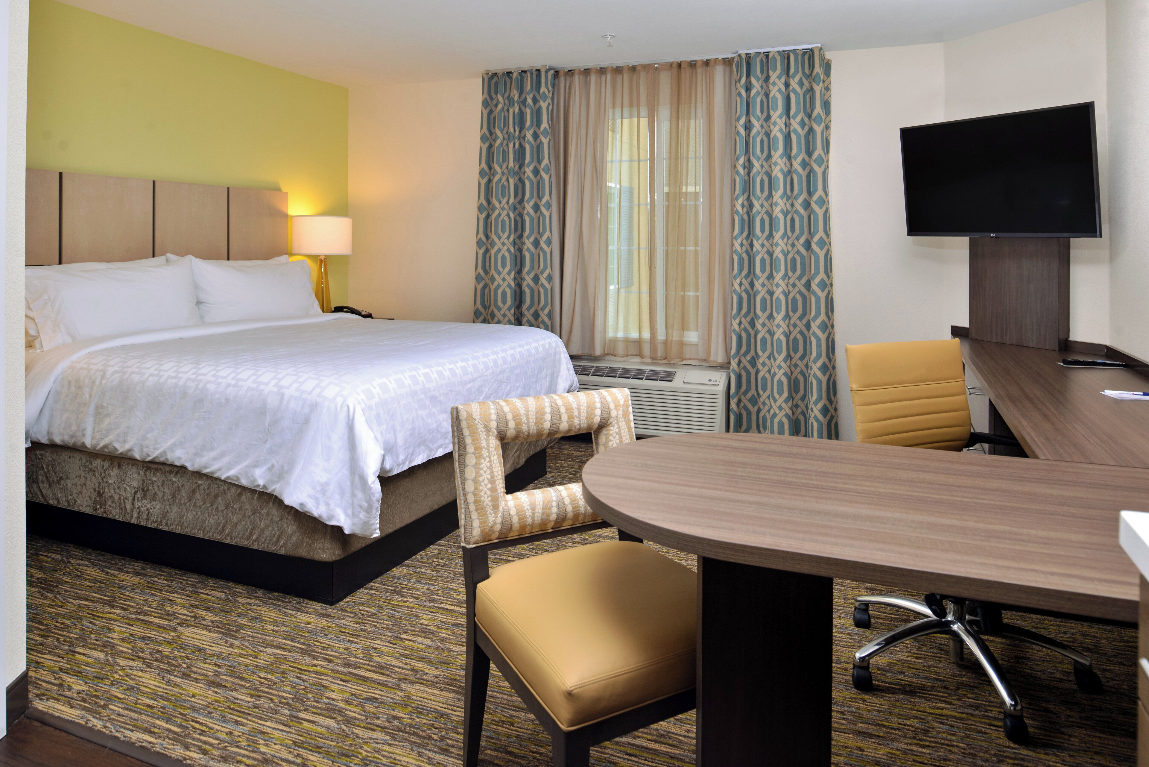 A hotel room with a bed, a desk, a chair, a television, and a window with curtains.