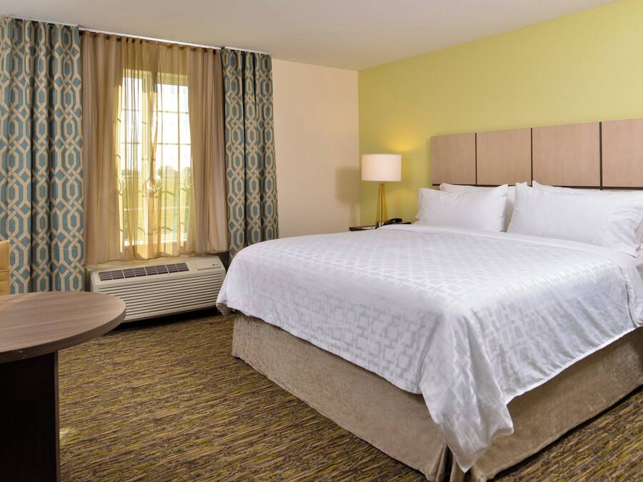 A hotel room with a bed, a bedside table, a lamp, a chair, and a window with curtains.
