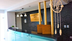 A reception desk with a glass partition, a wooden signboard, and a dreamcatcher decoration. - Mar Bohemio (Isla Mujeres)