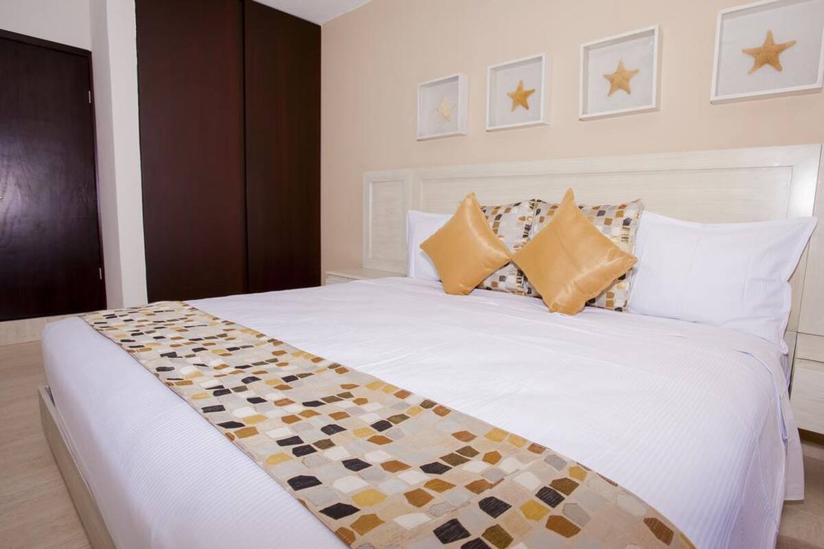 A neatly made bed with a patterned bedspread, a white headboard, and decorative pillows.