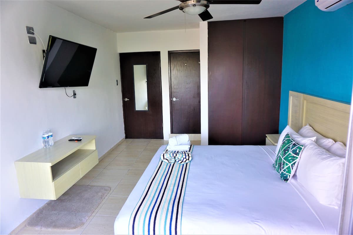 A hotel room with a bed, a TV mounted on the wall, a wooden nightstand, and a door.