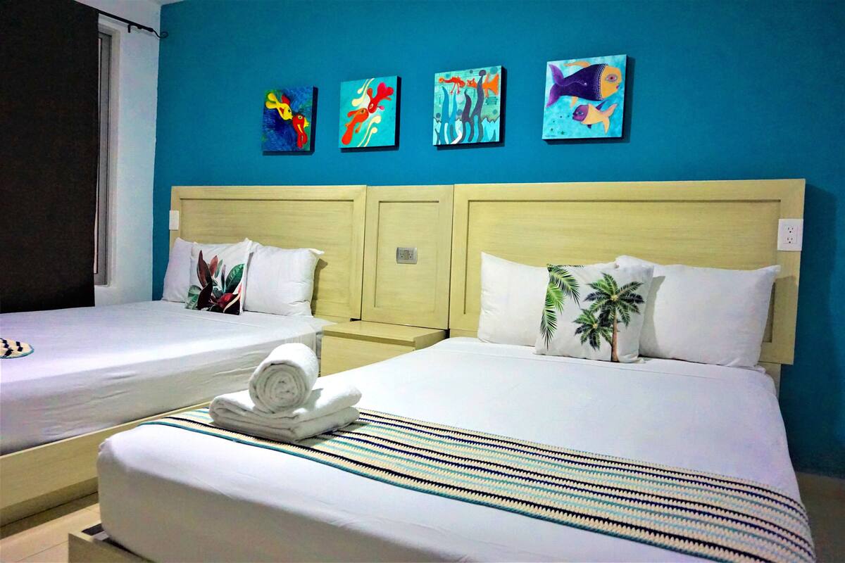 A hotel room with two beds, a blue wall, and four colorful paintings.