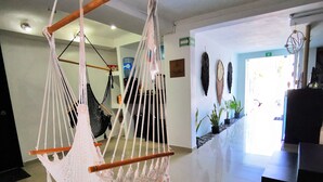 A room with a hammock chair, a water dispenser, and a wall with various decorations. - Mar Bohemio (Isla Mujeres)