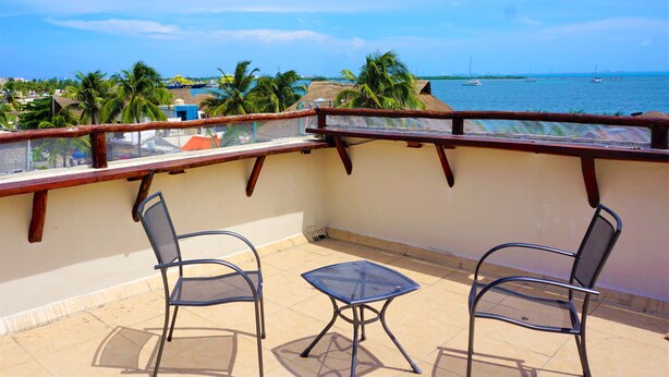 A balcony with two metal chairs and a small table, overlooking a beach with boats and palm trees. - Mar Bohemio (Isla Mujeres)