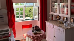 A kitchen with a window, red curtains, a table with a checkered tablecloth, and a cabinet with glass doors.