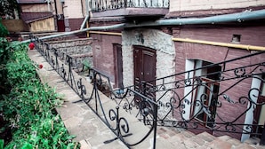 Un stretto sentiero in pietra con ringhiere in ferro battuto, affiancato da edifici con muri in mattoni rossi e porte in legno.