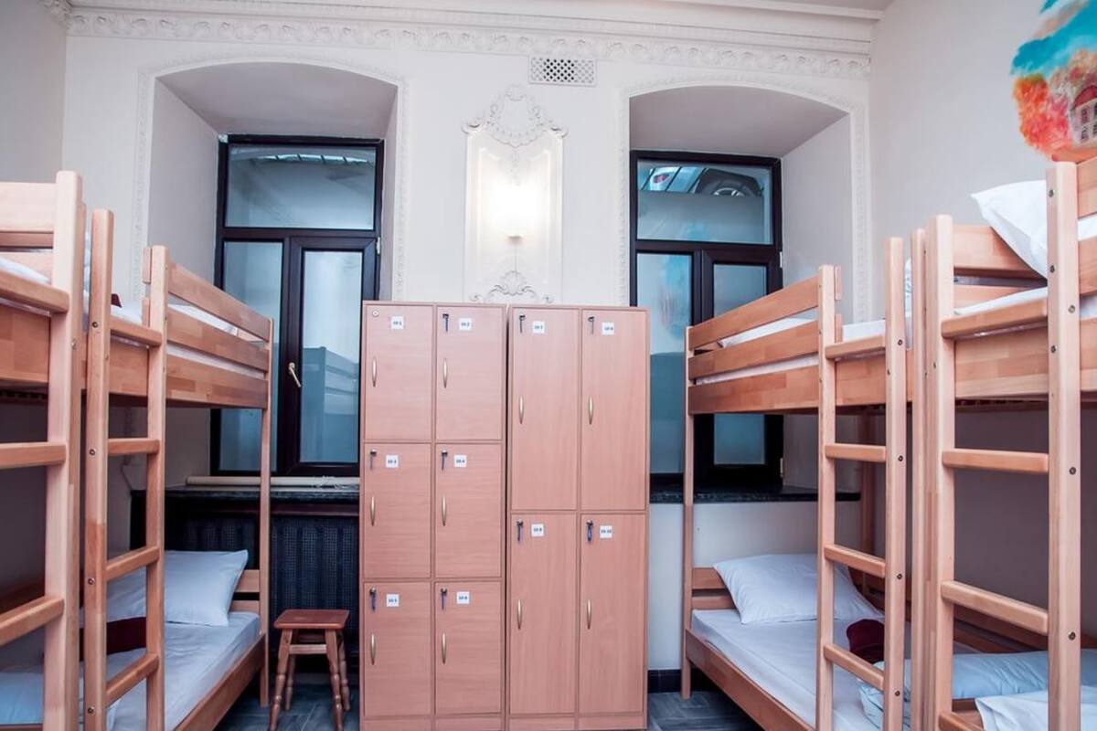 A dormitory room with bunk beds, a wardrobe, and a small stool.