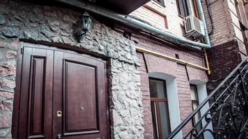 A stone facade with a large wooden door, a metal staircase, and a brick building with a window.