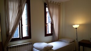 A small, single-bed room with a radiator, a bedside table with a cup, and a floor lamp.