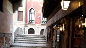 A narrow alleyway with stone steps leading to a building with a red facade and a sign reading "Fabbrica di Amare Formosa".