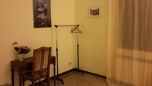 A corner room with a wooden chair, a small table, a floor lamp, and a painting on the wall.