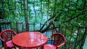 A red plastic table and chairs set on a balcony with a metal railing, surrounded by lush green foliage. - Golden Globus Hostel (Kyiv)