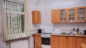A kitchen with wooden cabinets, a stove, and a window with blinds. - Golden Globus Hostel (Kyiv)