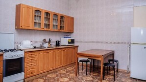 A kitchen with wooden cabinets, a stove, a microwave, and a dining table with chairs. - Golden Globus Hostel (Kyiv)