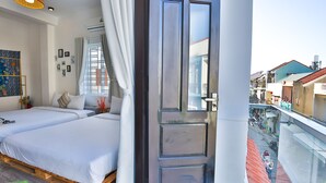 Un dormitorio con dos camas, un ventanal con cortinas y un balcón con vista a la calle.