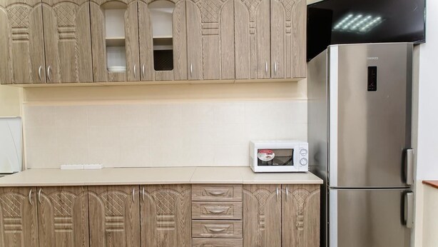 A kitchen with wooden cabinets, a stainless steel refrigerator, and a microwave on the countertop. - Globus Lipki Hostel (Kyiv)