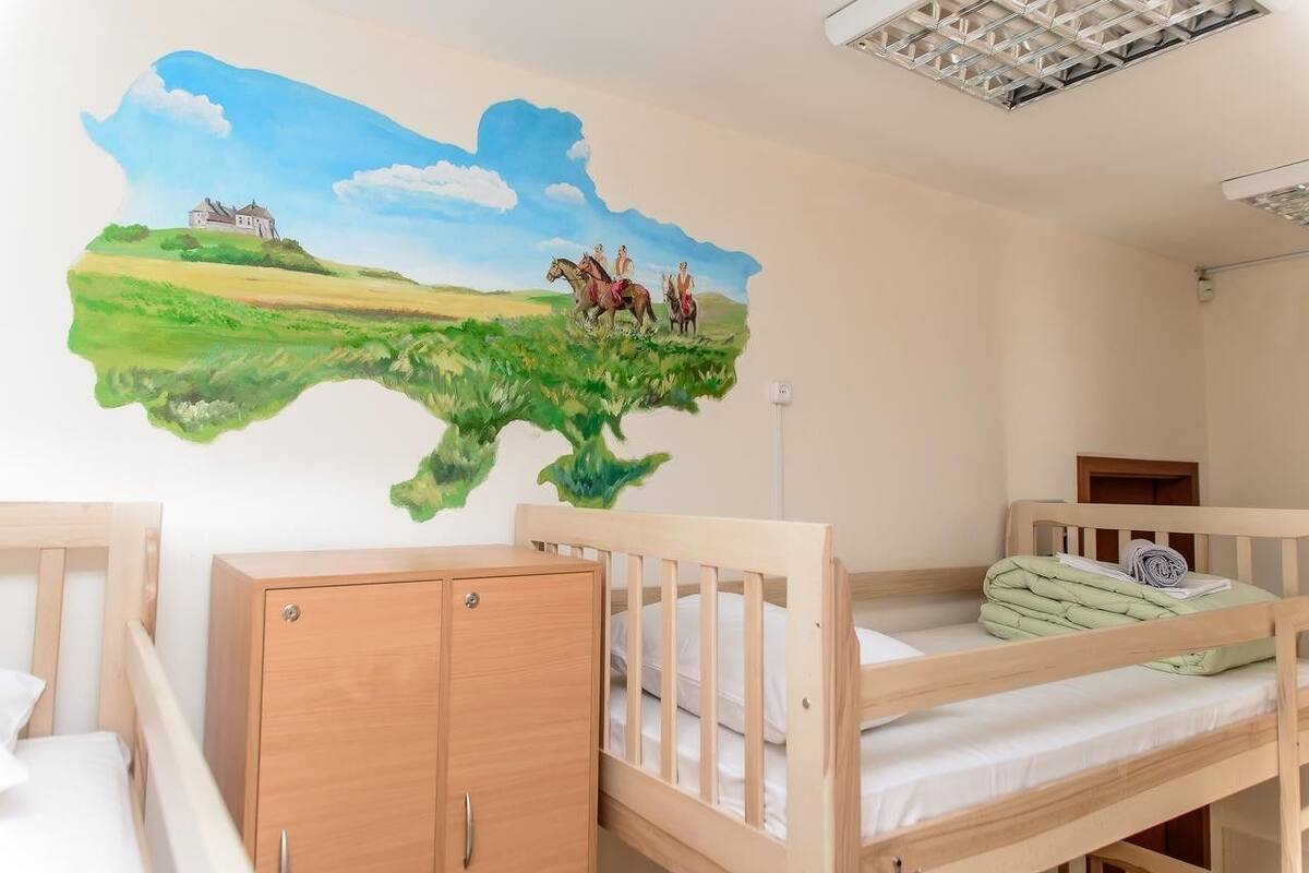A child's room with bunk beds, a wooden cabinet, and a mural of a landscape with a house and people on horseback.