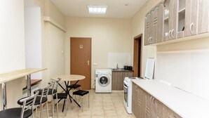 A compact kitchen with a washing machine, a sink, and a dining area with chairs and a table. - Globus Lipki Hostel (Kyiv)