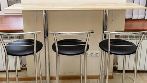 A kitchen with a white countertop, three black chairs with metal legs, and a tiled floor. - Globus Lipki Hostel (Kyiv)