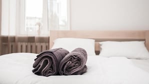 Una cama bien hecha con toallas enrolladas y almohadas blancas en una habitación de hotel con vista a edificios a través de la ventana.
