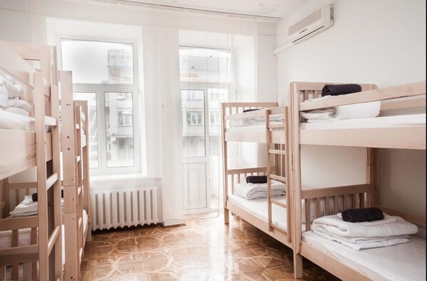 A dormitory room with bunk beds, a radiator, and a window with a view of buildings.