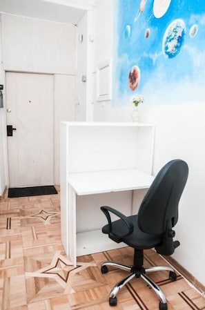 A room with a white desk, black office chair, and a wall with a space-themed mural.