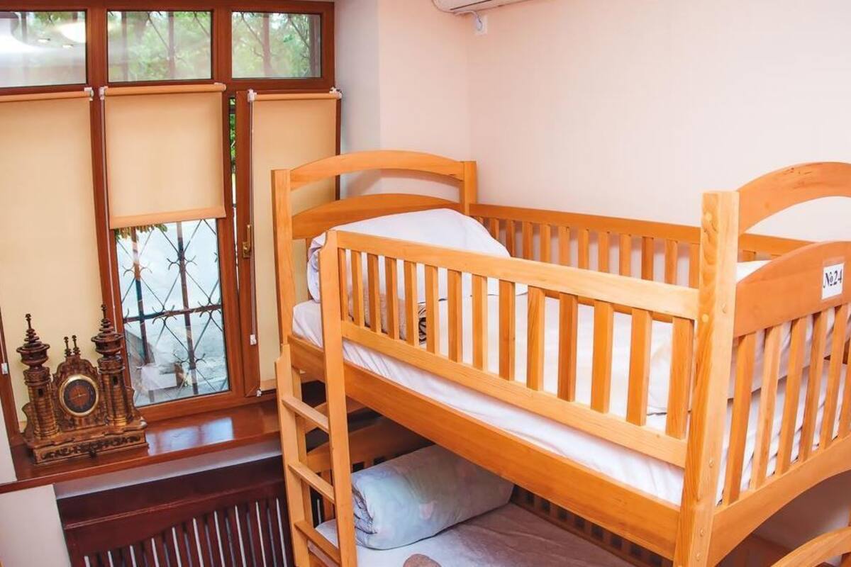 Una cama litera de madera con vista a la ventana, un reloj pequeño y un radiador.