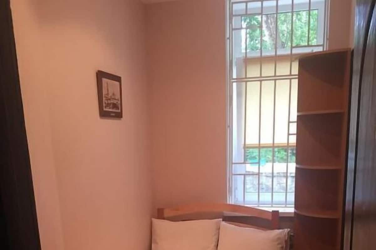 Una habitación pequeña y funcional con cama de madera, una mesita de noche y una ventana con rejas.