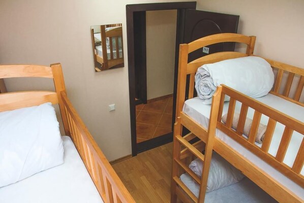 Una habitación con dos literas de madera, un espejo pequeño en la pared y una puerta que da a otra habitación.