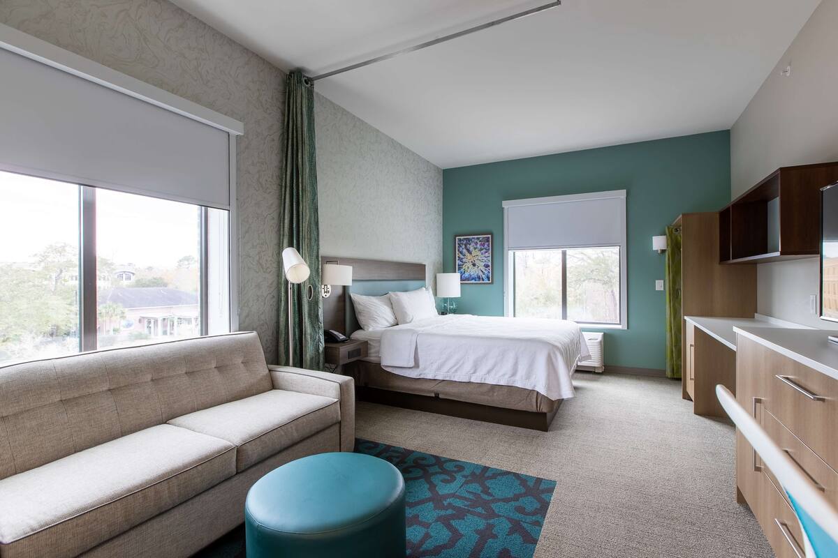 A hotel room with a bed, a sofa, a desk, and a TV.