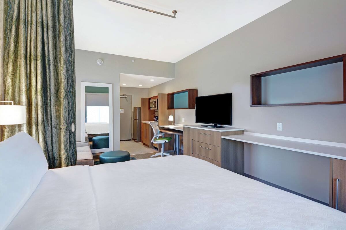 A hotel room with a large bed, a desk with a chair, a television, and a bathroom visible in the background.