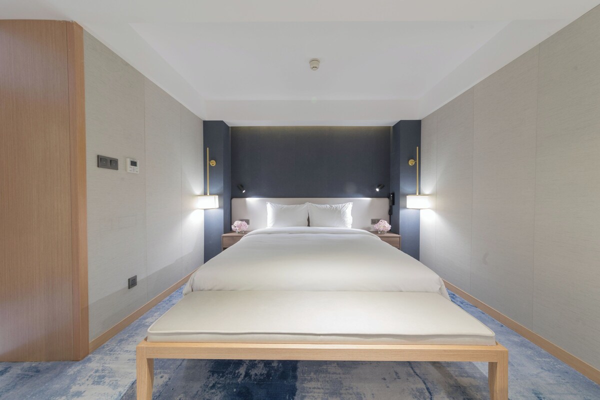 Habitació d'hotel moderna amb un llit gran, làmpades laterals i un paviment de fusta.