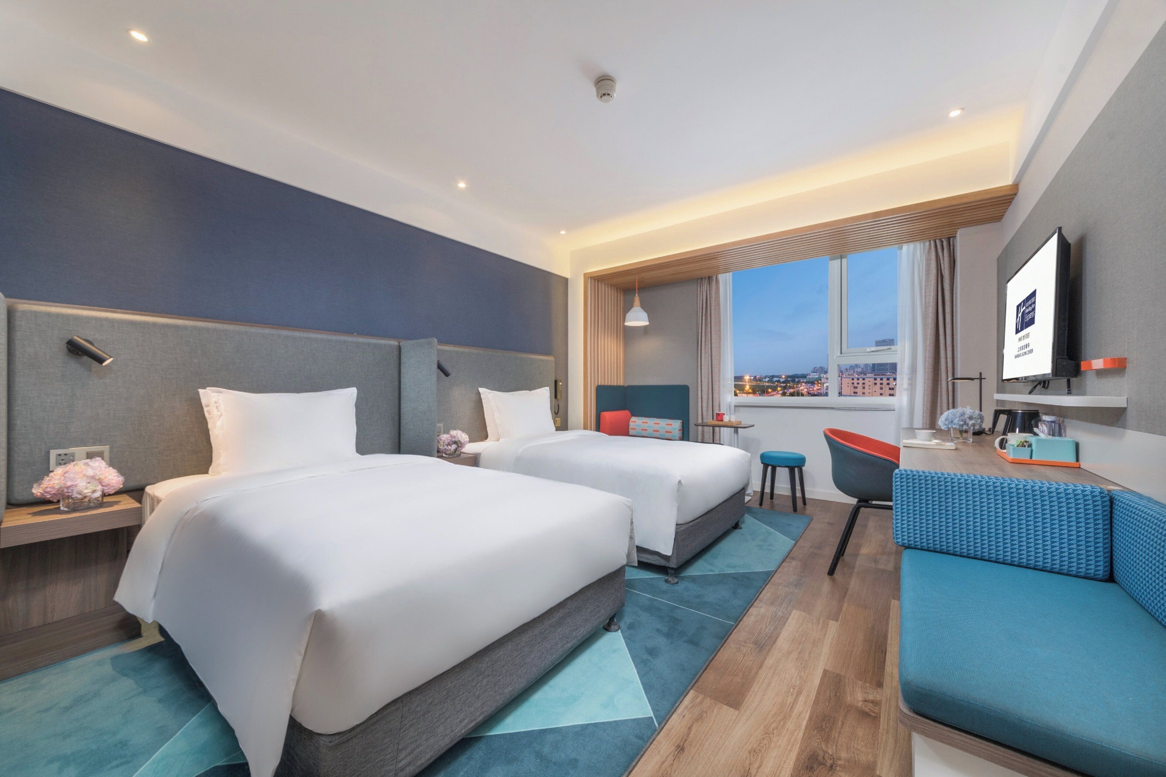 Habitación de hotel con dos camas, un sofá, un televisor y una ventana con vista a la ciudad.