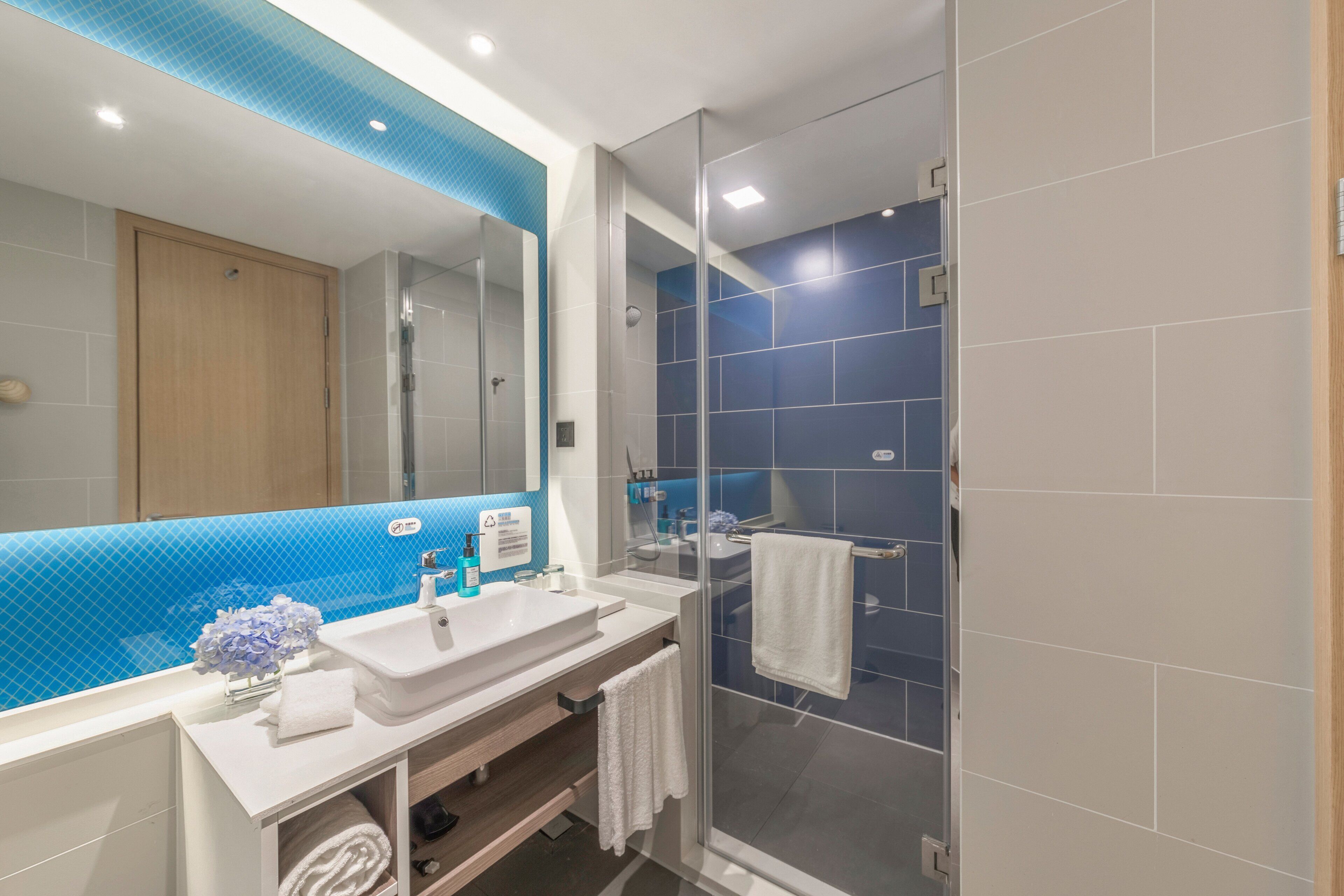 A modern bathroom with a glass shower enclosure, a white sink, and a blue-tiled shower wall.