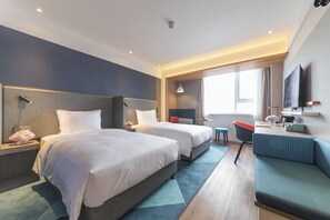 Ein Hotelzimmer mit zwei Betten, einem Schlafsofa, einem Schreibtisch und einem Fernseher.