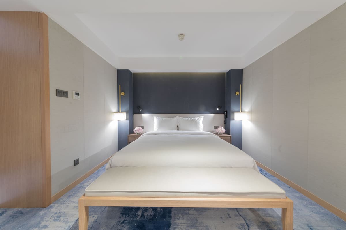 A modern hotel room with a large bed, bedside lamps, and a wooden floor.