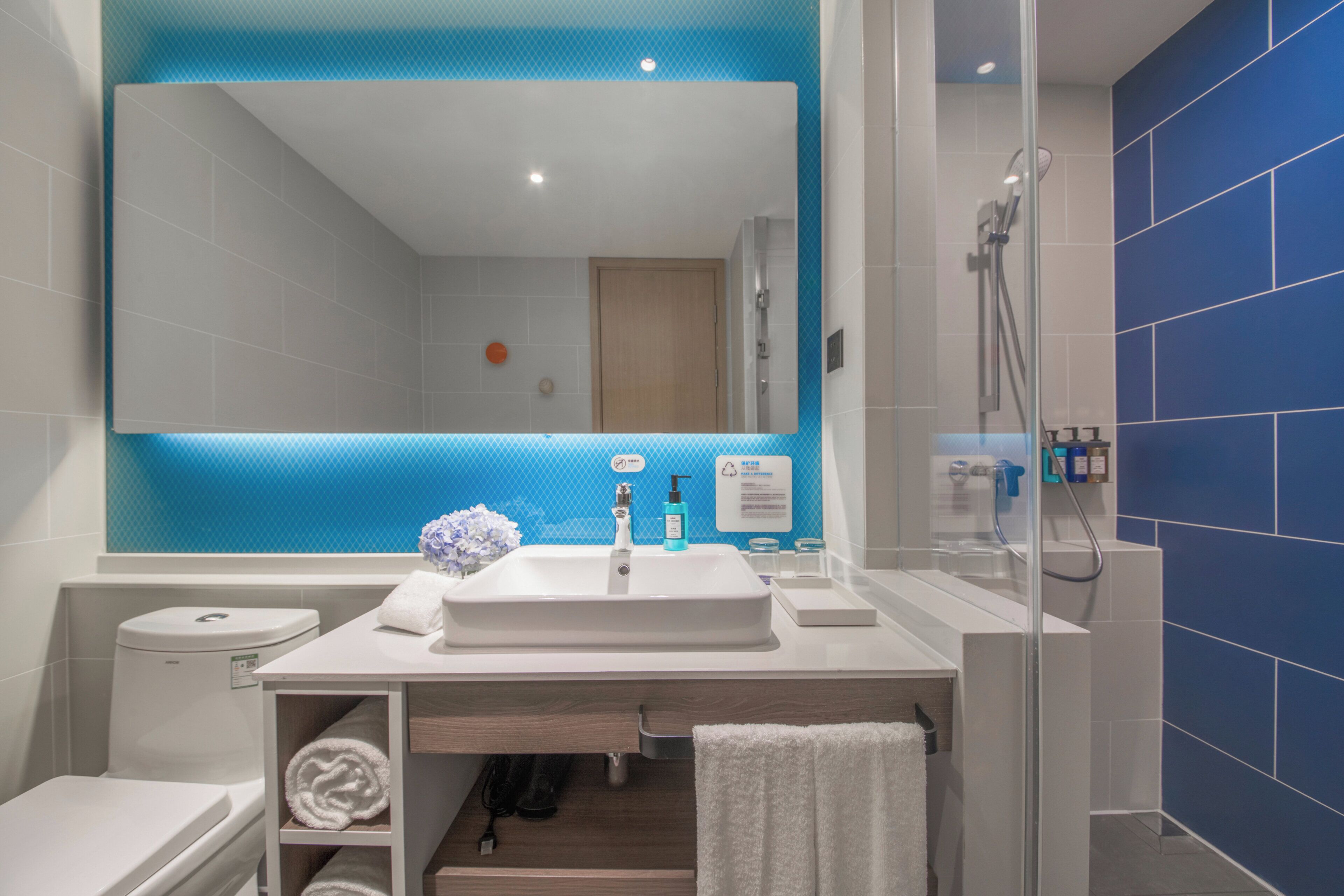 A modern bathroom with a white sink, a mirror, a shower, and blue-tiled walls.
