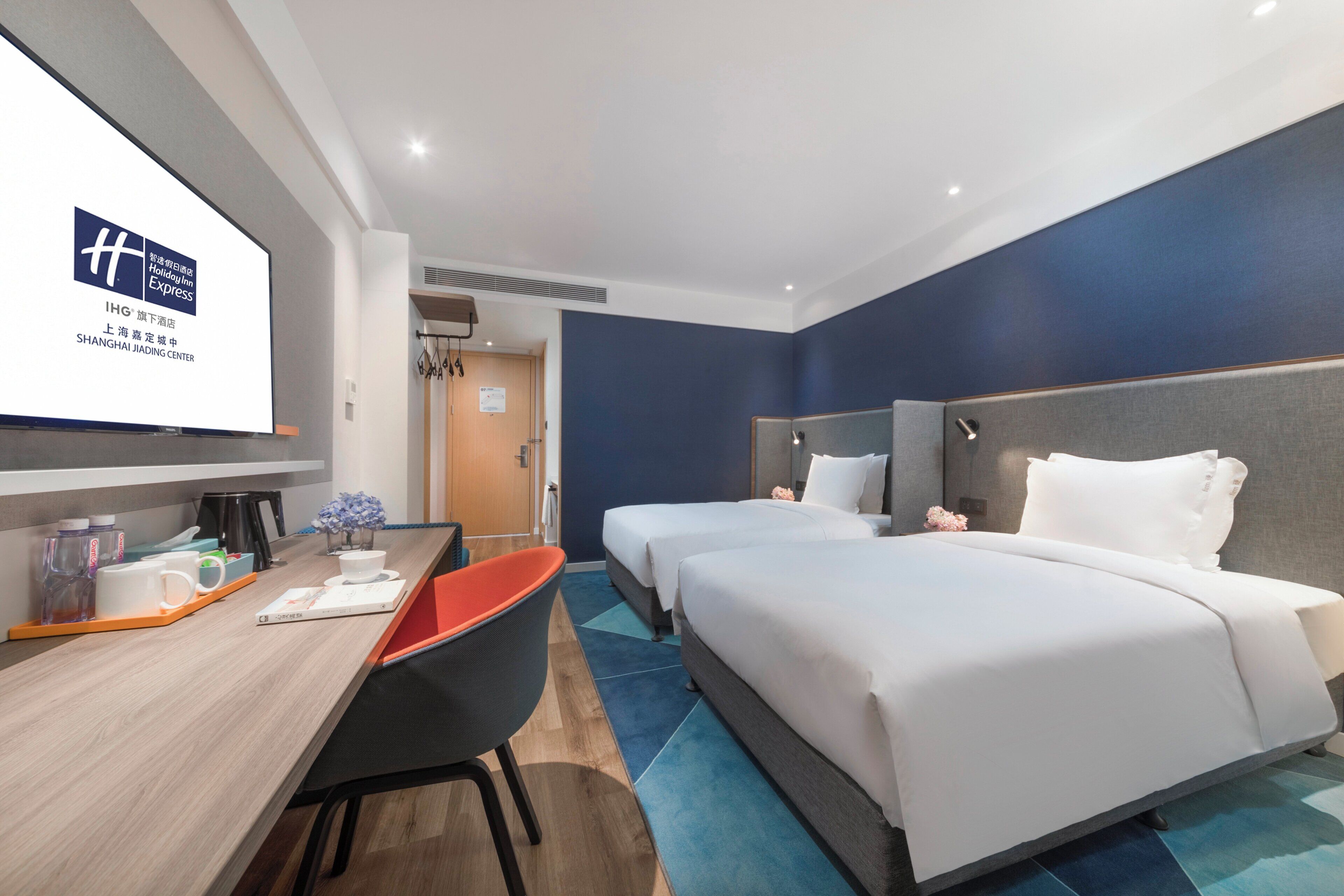 Habitación de hotel con dos camas, un escritorio con silla, una pantalla de televisión y la puerta del baño.